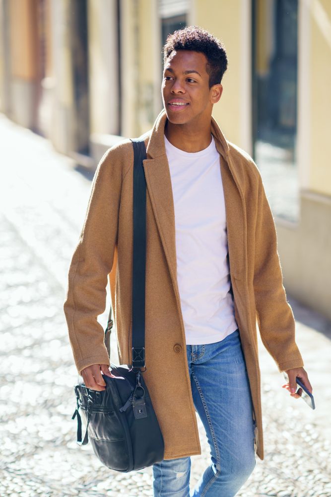 Cuban male walking down street with leather bag and phone