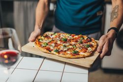 Man laying pizza on wooden board of kitchen counter with red wine