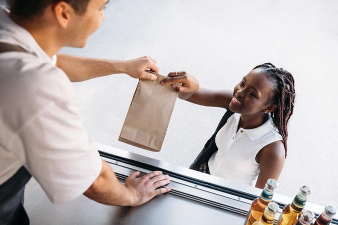 Woman picking up food in paper bag from smiling vendor