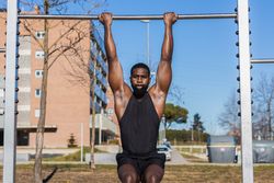 Strong Black sportsman working out on bar in town
