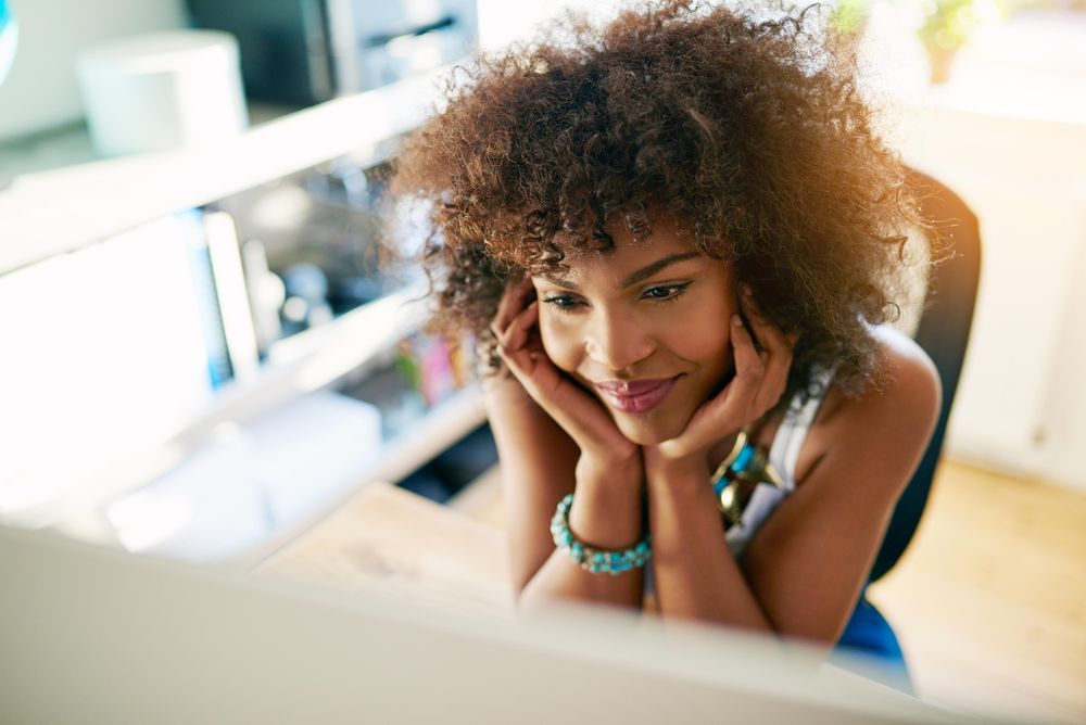 Looking down at Black female at her home office desk reading computer screen