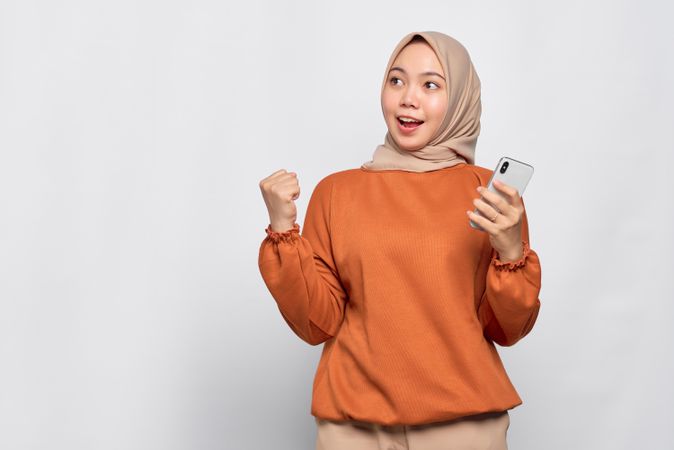 Surprised Muslim woman celebrating a win while holding her smartphone