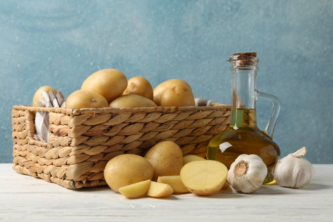 Side view of potatoes, olive oil and garlic next to wicker basket