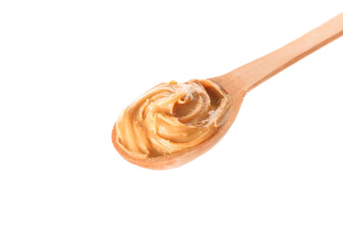 Creamy peanut butter in wooden spoon isolated on light background, closeup. A traditional product of American cuisine