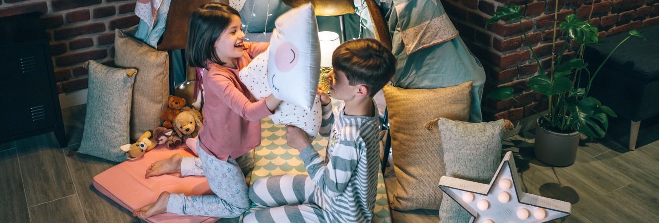 Banner of happy siblings having fun in pillow fight at living room. Domestic family life concept.