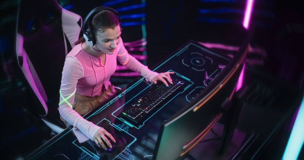 Young Woman Wearing Futuristic Pink Clothes and Neon Rings, Playing Video Games on a Desktop Computer.