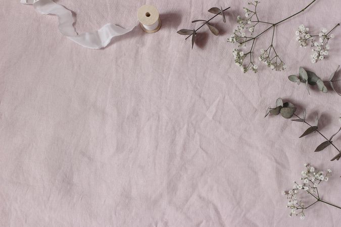 Floral wedding, birthday table composition. Gypsophila, eucalyptus tree leaves leaves and silk ribbons on pink linen table cloth background. Flat lay, top view. Copy space, no people.
