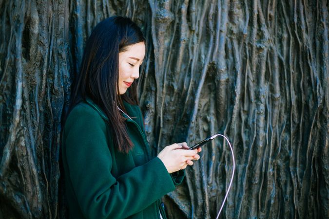 Asian female listening to music near rough wall