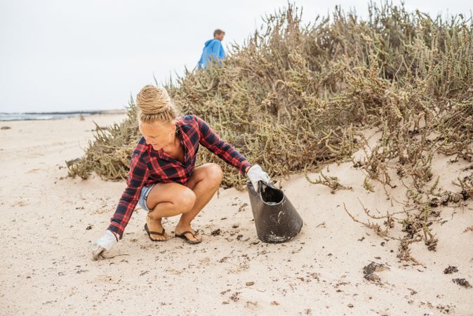 Content modern woman picking litter from sandy seashore