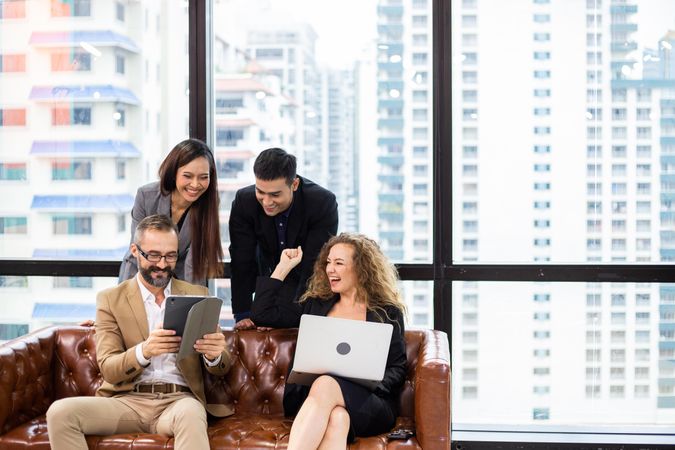 Group of cheerful businesspeople sitting on couch watching project on computer tablet