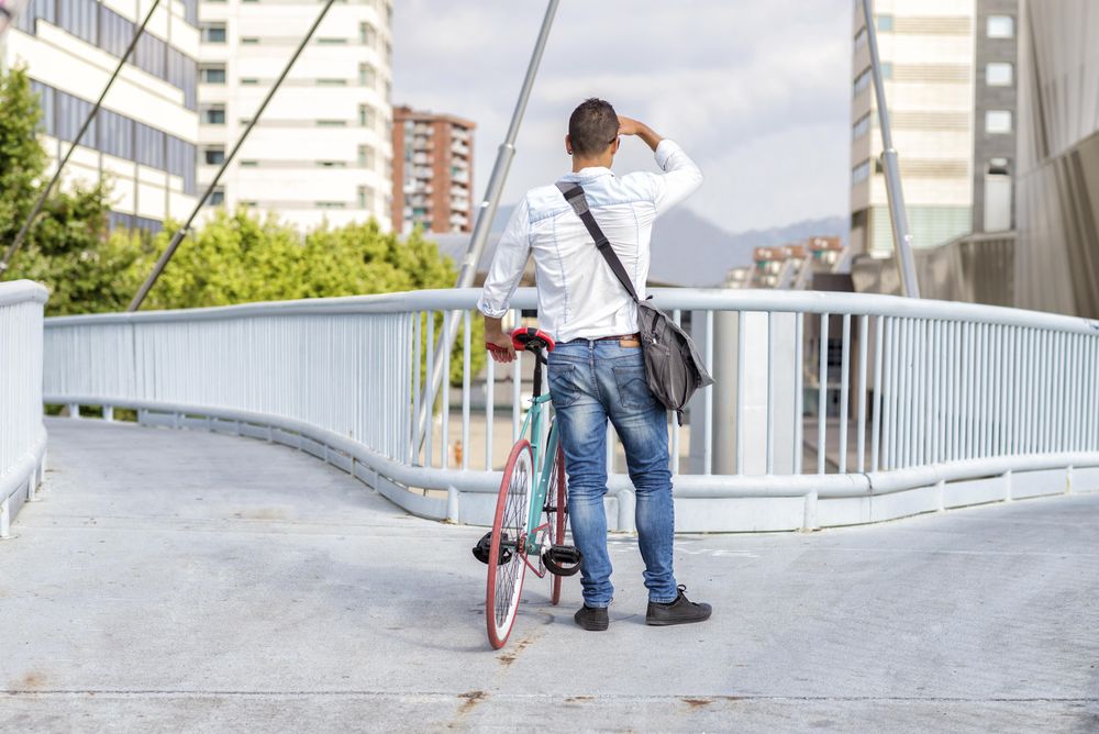 Male with bike looking over city view from bridge