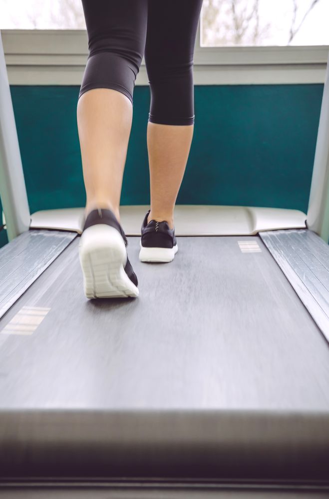 Legs of woman in leggings and trainers walking on treadmill