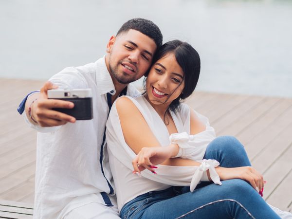 Woman with man taking photo selfie and kissing on bench