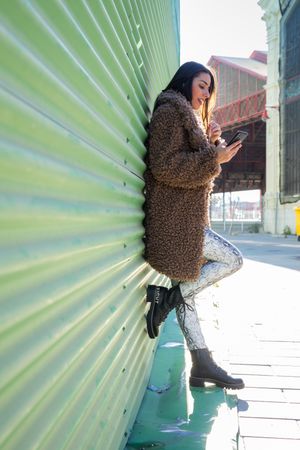 Trendy woman with smartphone near wall