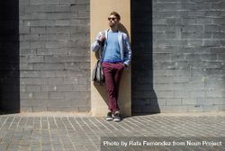 Man wearing casual clothes while leaning on a building wall outside with bag 0WOVay