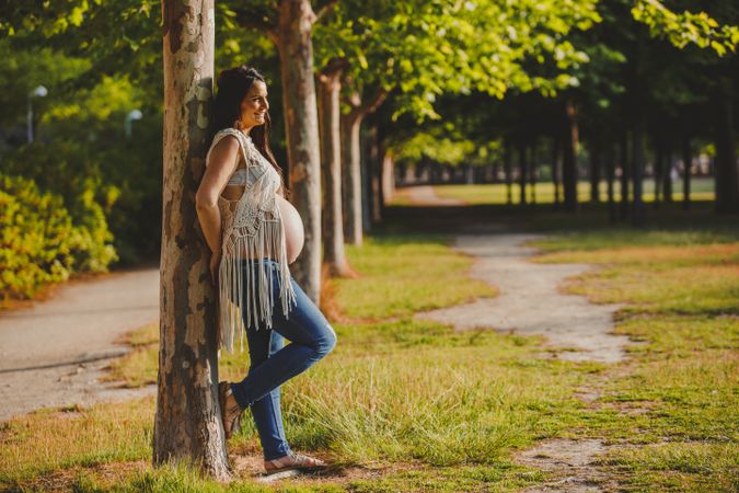 Pregnant female leaning on tree in park