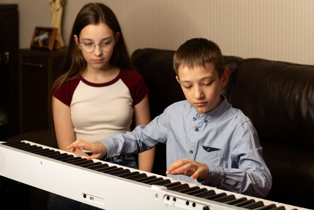 Girl watching as boy plays the keyboard with concentration.