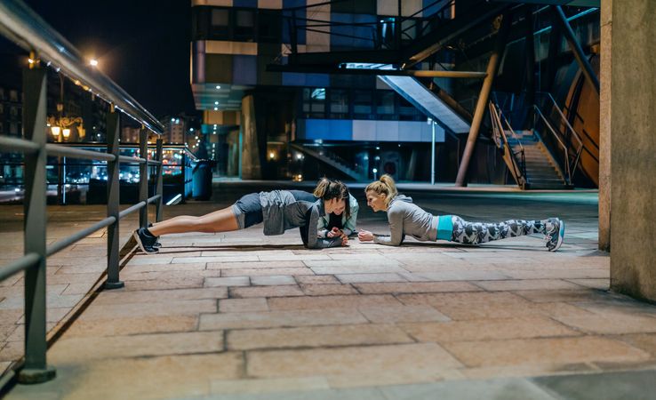 Women's sport team doing plank exercises training in city at night
