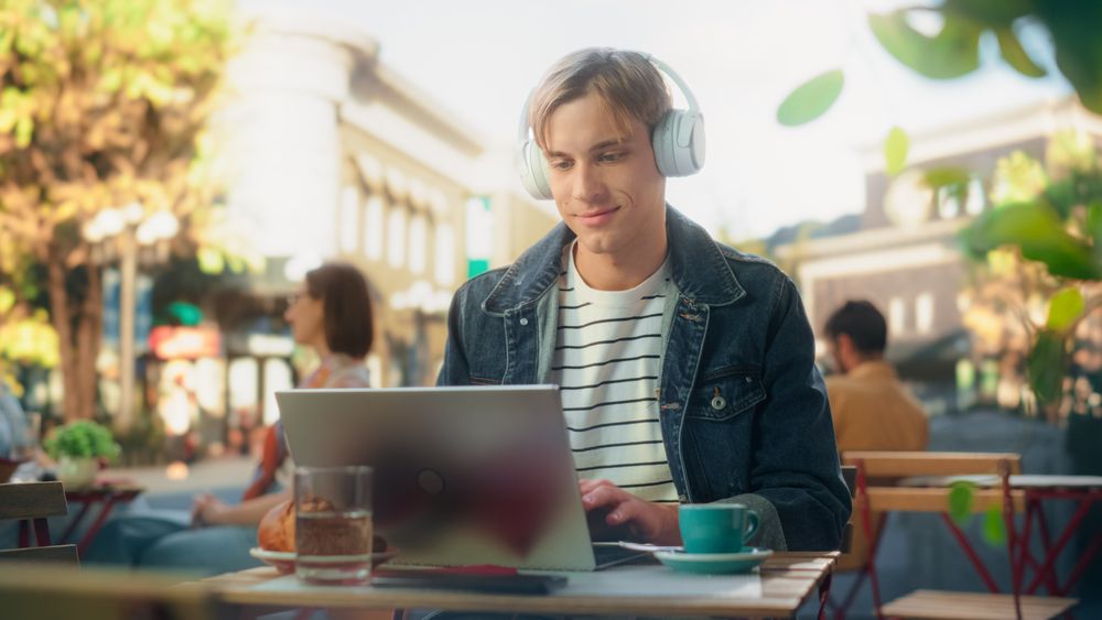 Freelancer Wearing White Headphones and Using a Laptop Computer for Remote Online Work in the City.