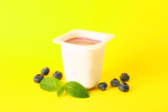 Plastic cup with yogurt on color background, space for text