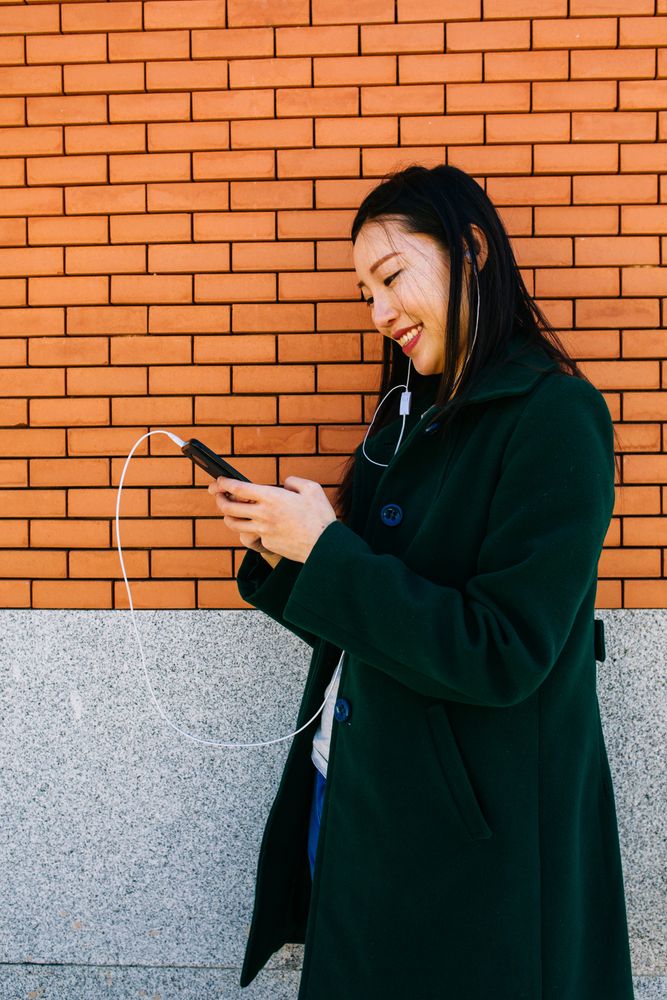 Asian female listening to music near brick wall