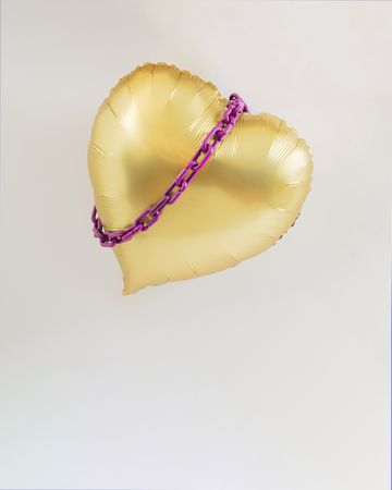 Gold heart balloon in the air with violet purple chains around it