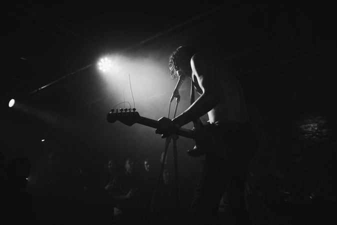 Young male rock musician singing on stage with guitar and spotlight
