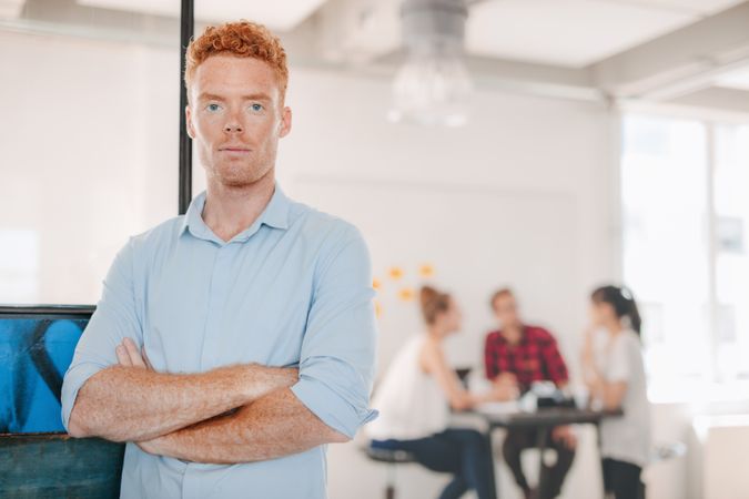 Confident man in casual business clothes stands with coworkers in background