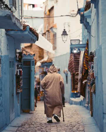 Back view of Moroccan man in djellaba with hood walking in the alley of Chefchaouen, Morocco
