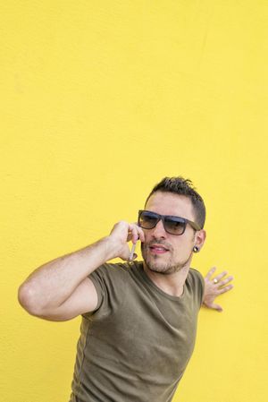 Male leaning on yellow wall talking on cell phone
