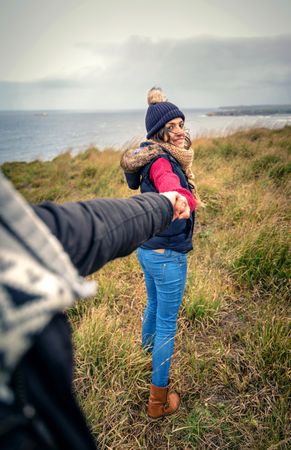 Woman in warm jacket and scarf leads her partner to the ocean