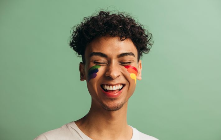Close-up of a cheerful young man with pride flag painted on face