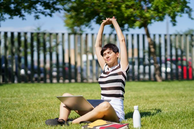 Woman stretching in park with computer on lap