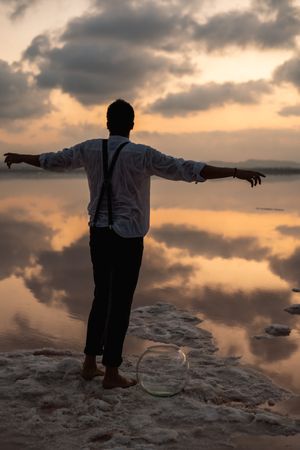 Relaxed man standing with outstretched hands with empty fish tank at shore