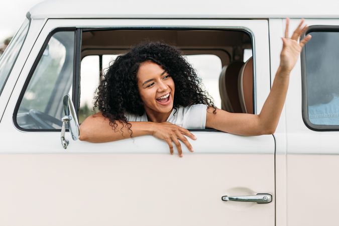 Smiling woman with curly hair waving out of a car window