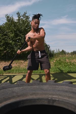 Muscular Black guy hammering tire in outdoor gym