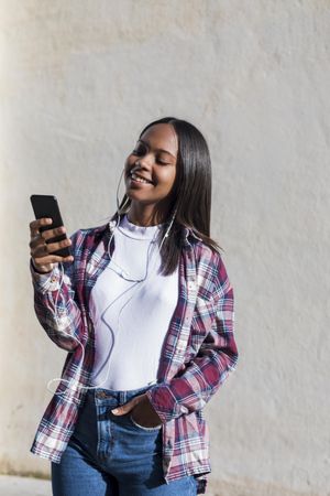 Female standing in the sun in front of wall smiling at phone