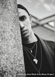 Monochrome shot of man in Africa necklace looking out behind wall 0gaMj4