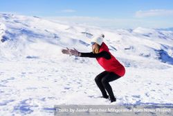 Woman in snow gear doing squats on snowy mountain bGRvRX