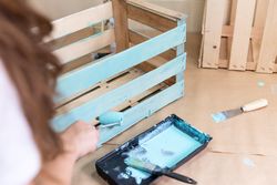 Woman paining wooden box in blue color with roller