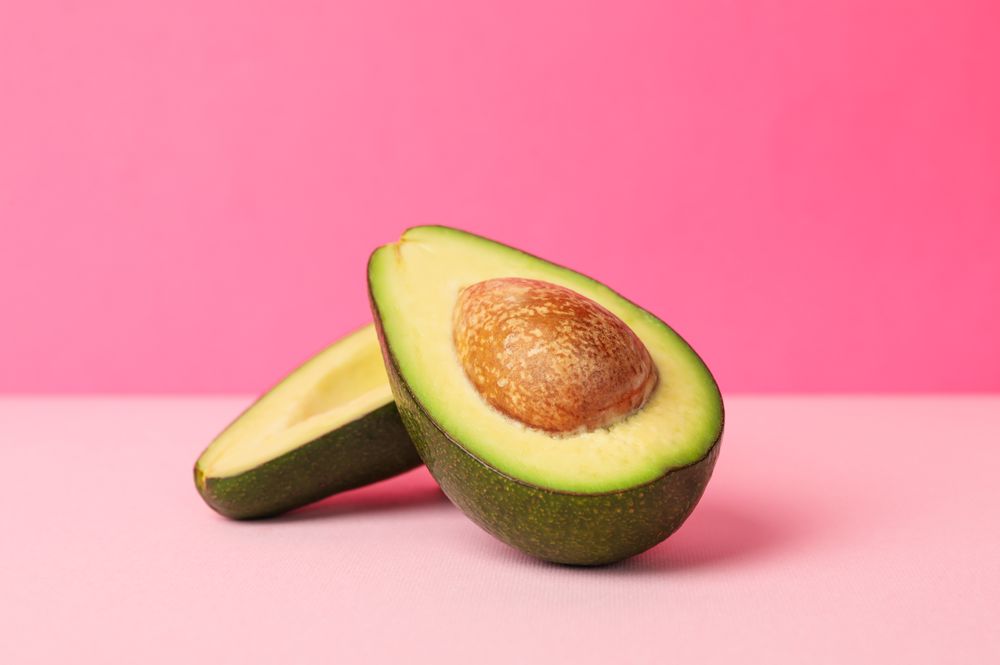 Ripe fresh avocado on pink background, space for text
