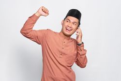 Smiling Muslim man in kufi hat gets good news on smart phone