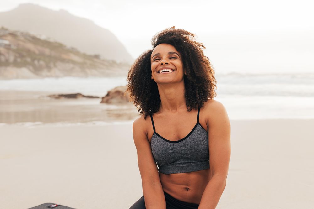 Happy woman sitting on beach in workout gear