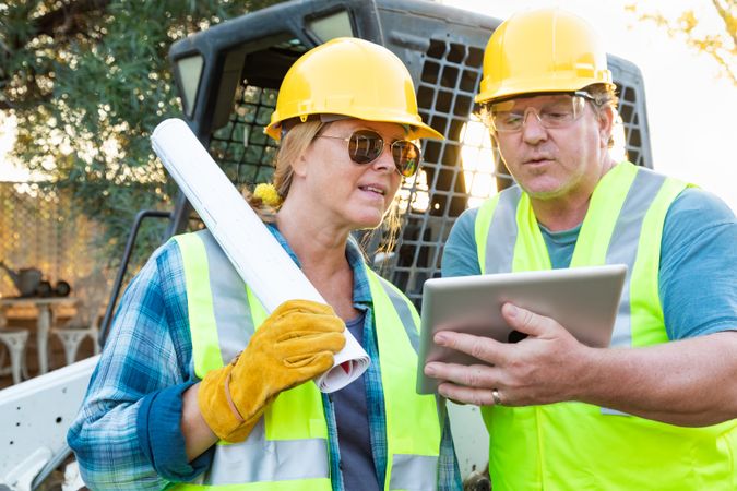 Male and Female Workers With Technical Blueprints and Computer Tablet Talking at Construction Site