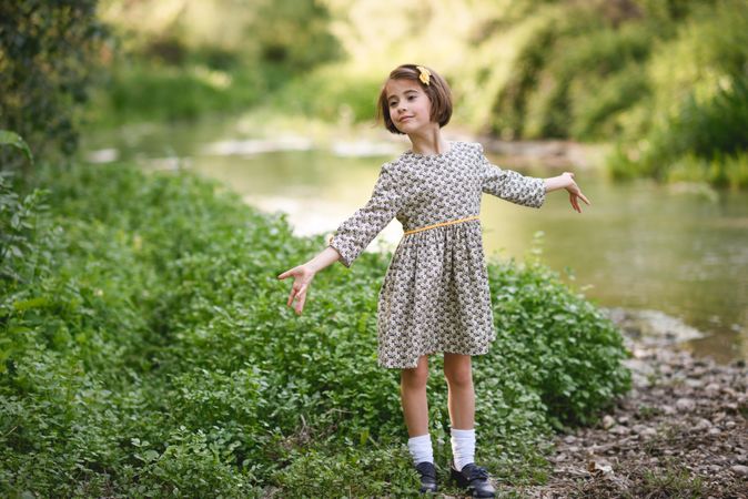 Child in dress looking away from the river with her arms open