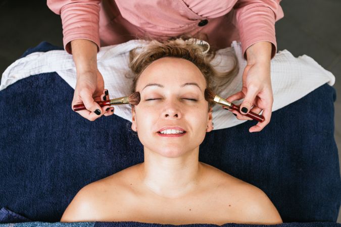Crop visagiste doing makeup for woman in beauty salon