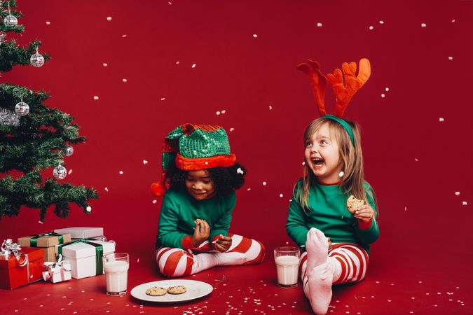 Joyful little kids enjoying snow flakes falling while eating cookies with milk