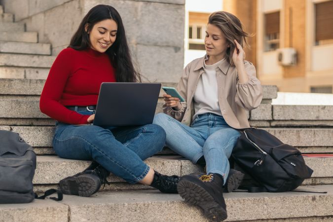 Two students sitting on the stairs of the college with the laptop and the mobile