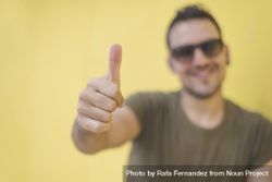 Smiling male with thumbs up in front of yellow wall outside 0WqdP4