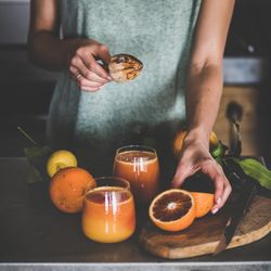 Woman holding squeezer with freshly squeezed blood orange juice, square crop